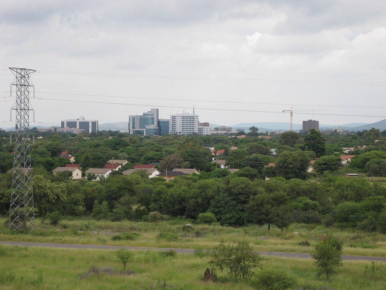 Office towers of central Gaborone rising above green suburbs and an electricity pylon under an overcast sky