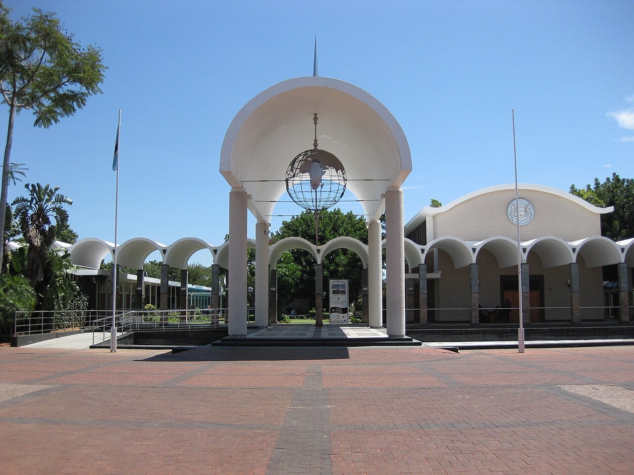 The Parliament building in Gaborone with a white arched portico, a globe sculpture and the Botswana flag