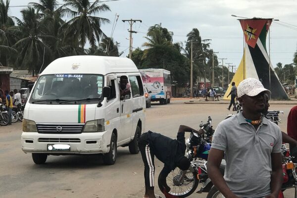 A white minibus, motorbike taxis and a tall monument painted in the colours of Mozambique's flag on a street in Pemba