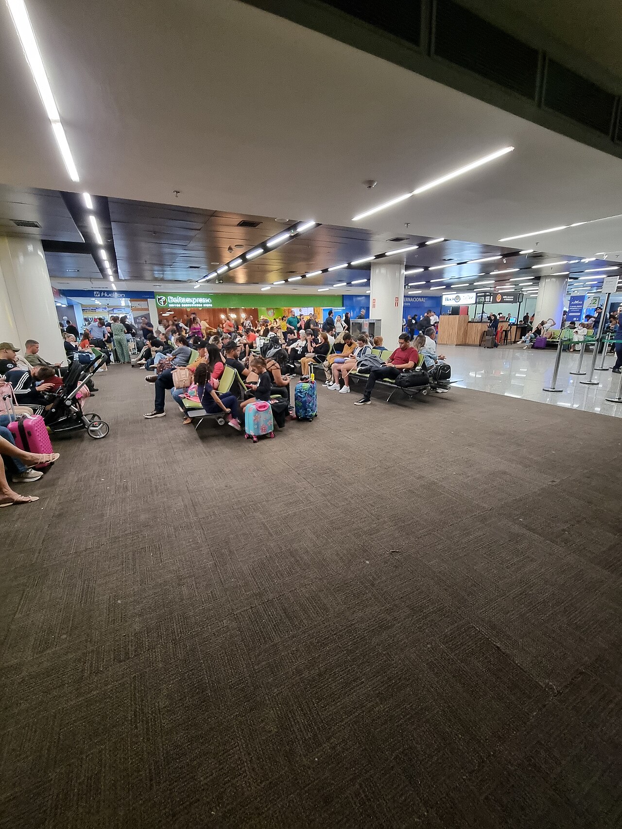 Passengers with suitcases and children waiting on rows of seats in the departure area of Brasília International Airport