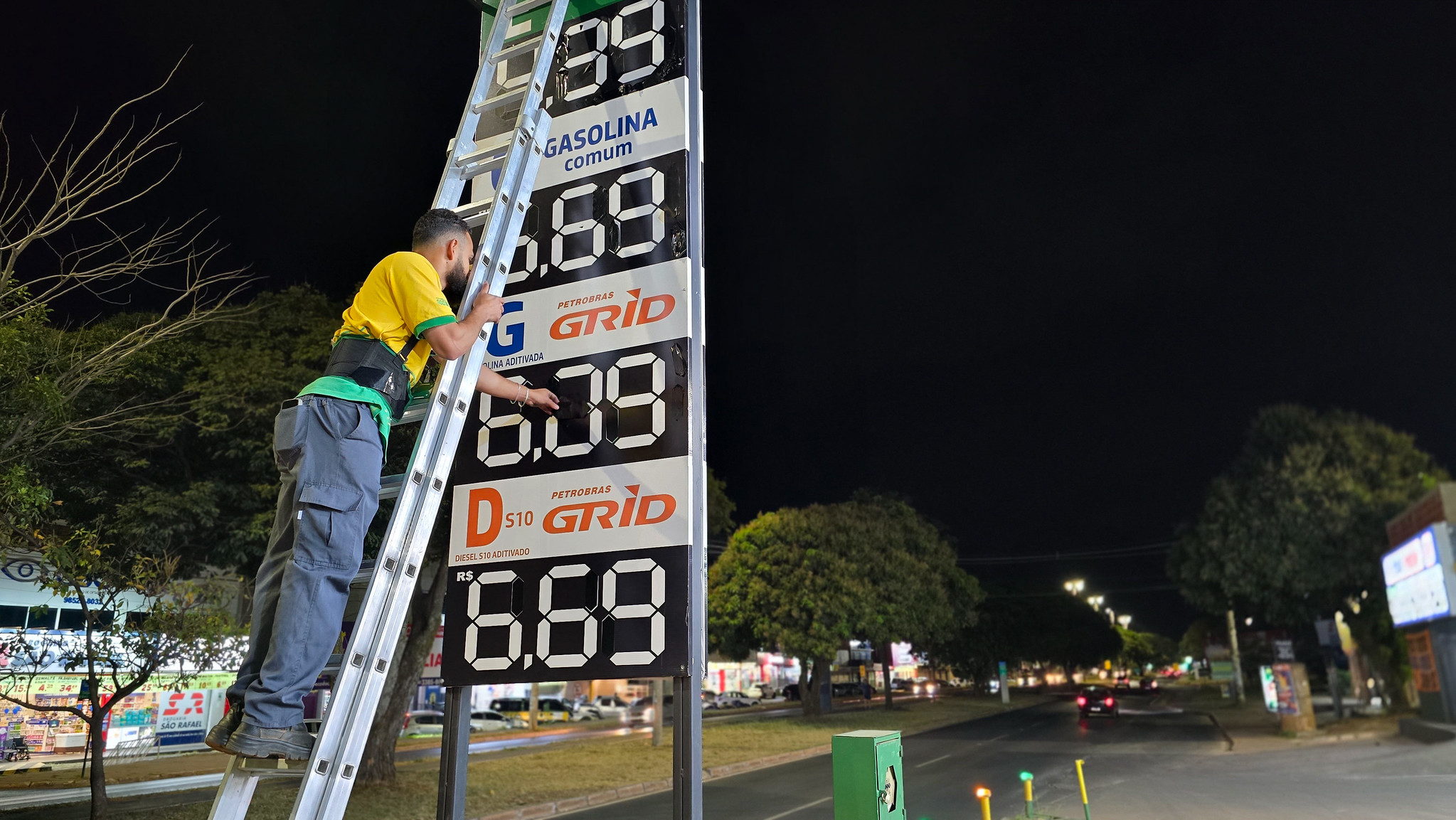 A worker on a ladder adjusts the fuel price board at a petrol station in Brasília at night