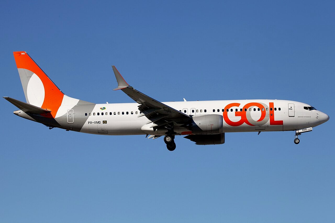 A white Gol Boeing 737 MAX 8 with an orange tail and orange GOL lettering on approach against a clear blue sky