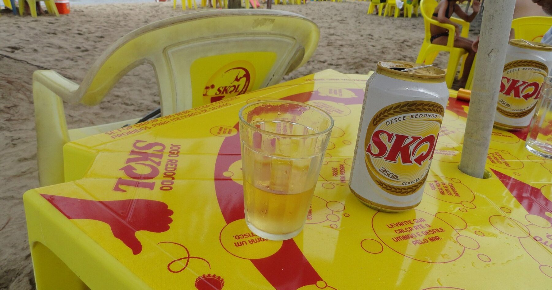 A can of Skol beer and a glass on a yellow Skol-branded table at a beach kiosk in Brazil