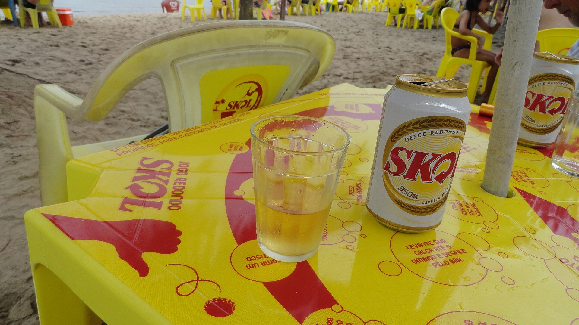 A can of Skol beer and a glass on a yellow Skol-branded table at a beach kiosk in Brazil