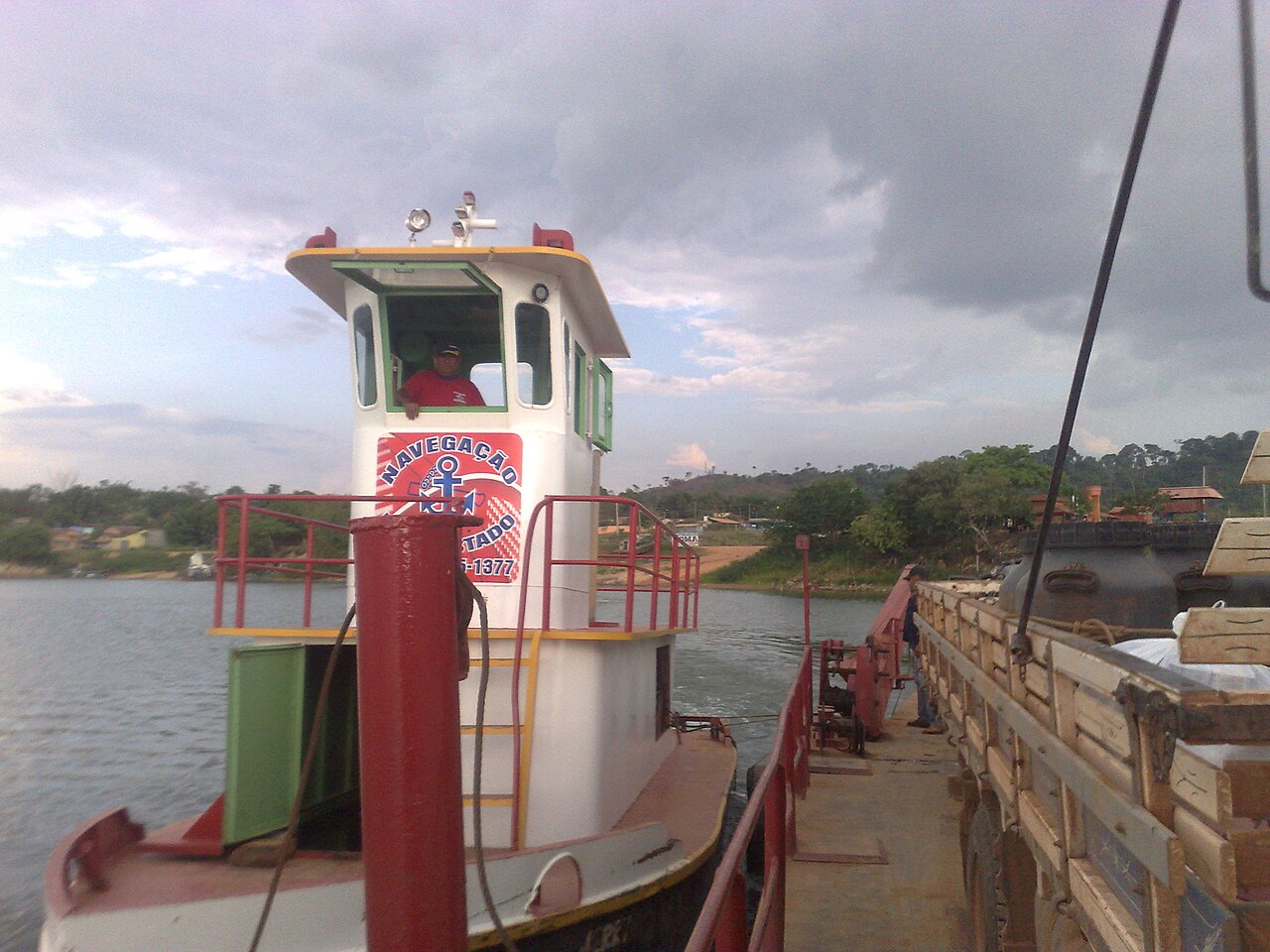 A tugboat and ferry barge carrying a loaded truck on the Xingu River, with wooded banks behind