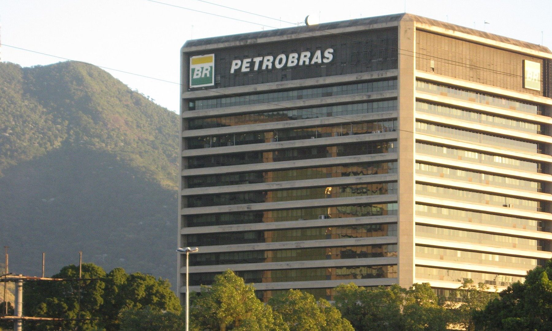 A Petrobras office tower in Rio de Janeiro with the company name and logo on its roof, in front of a forested hill