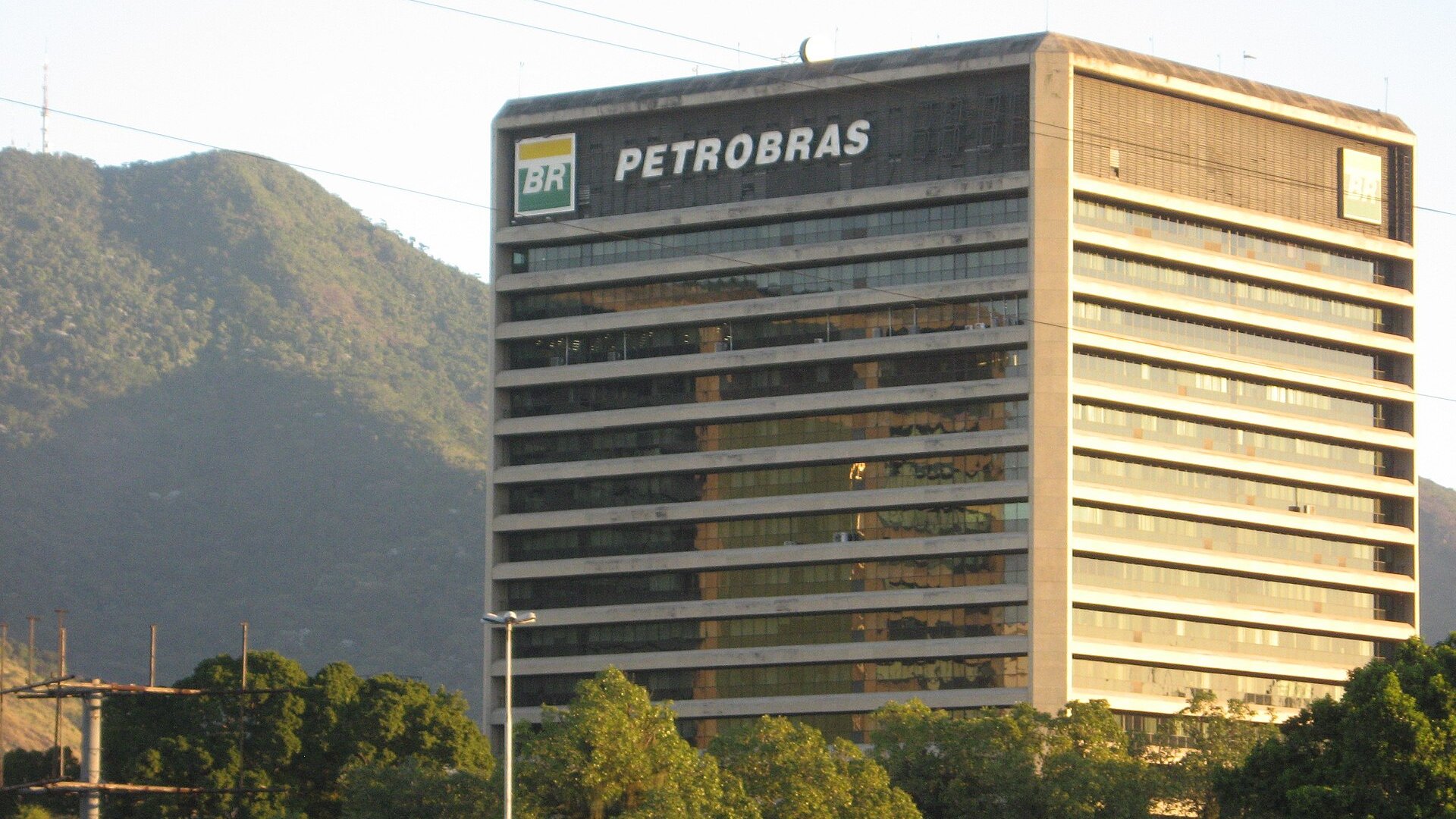 A Petrobras office tower in Rio de Janeiro with the company name and logo on its roof, in front of a forested hill