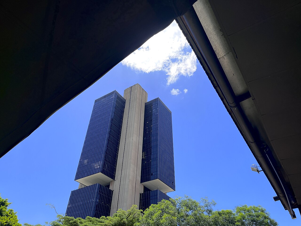 The Banco Central do Brasil tower framed by a concrete overpass in Brasília, seen from below