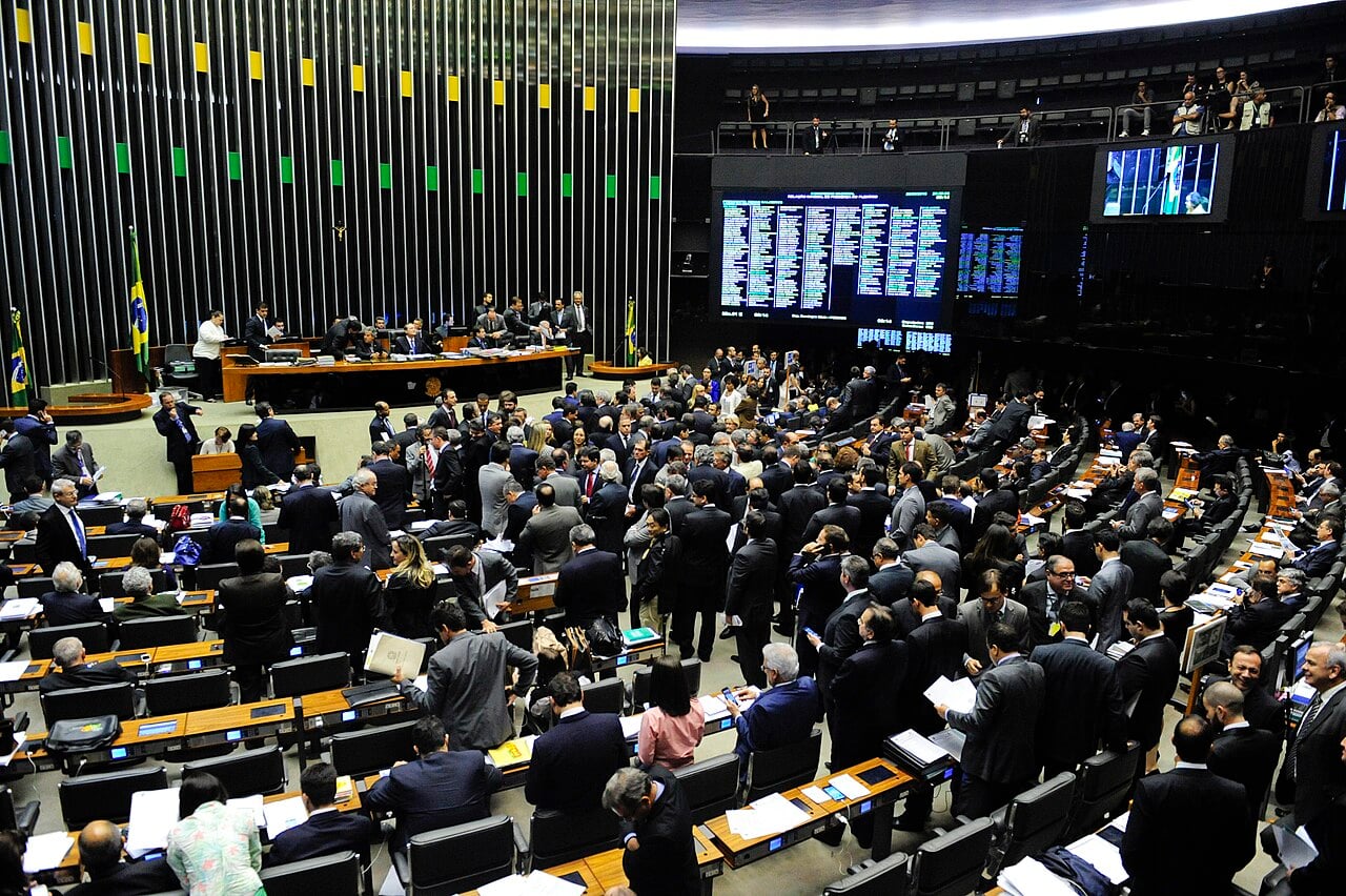 Lawmakers crowd the floor of the Chamber of Deputies plenary in Brasília beneath a large electronic vote board