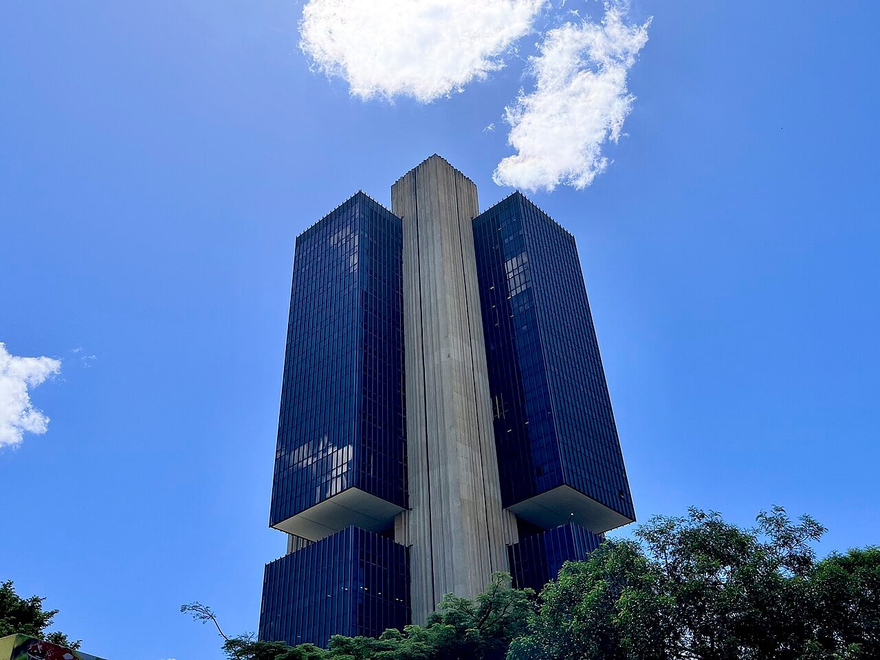 Dark glass towers of the Banco Central do Brasil headquarters in Brasília under a blue sky with trees in front