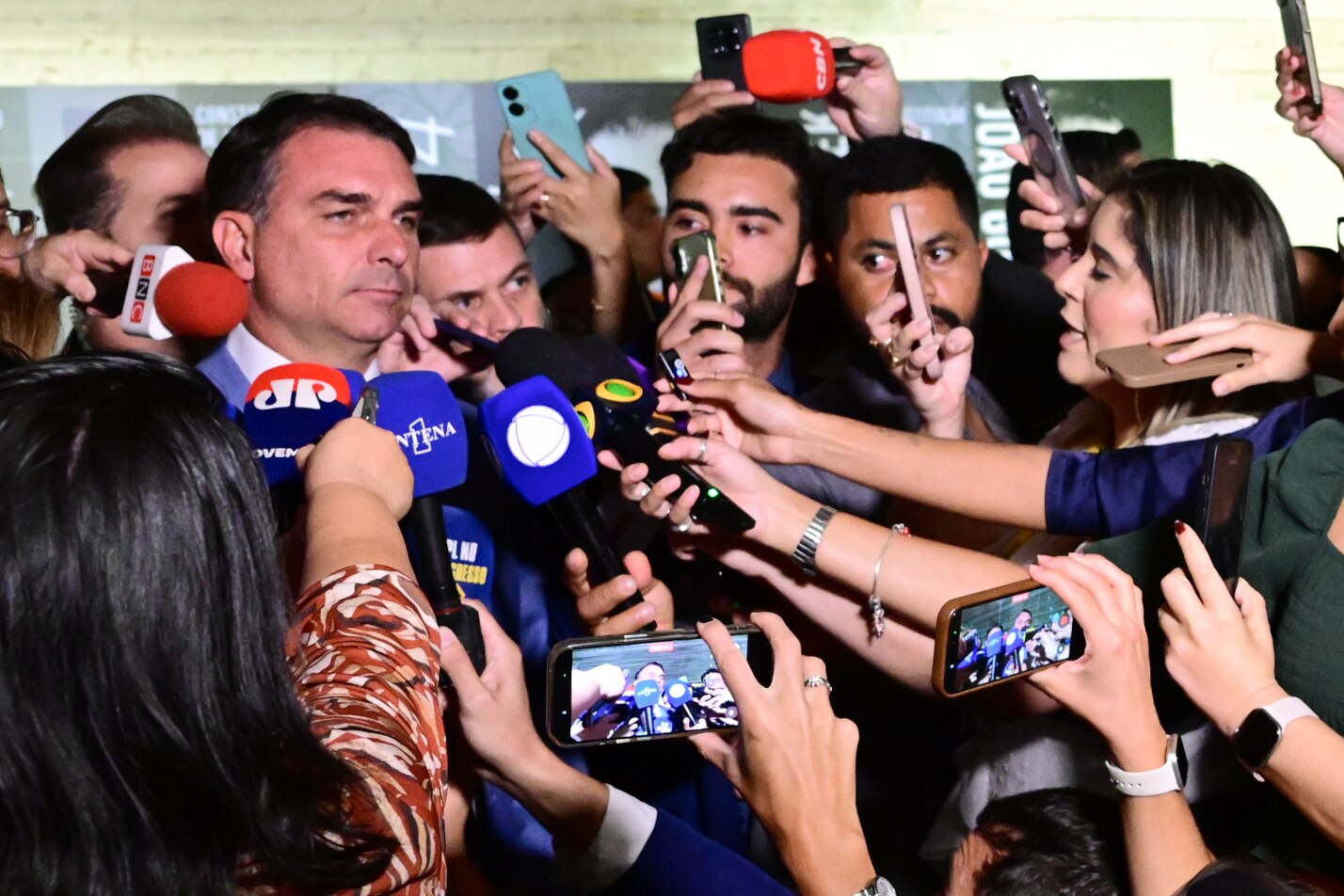 Senator Flávio Bolsonaro surrounded by reporters holding microphones and phones as he gives an interview