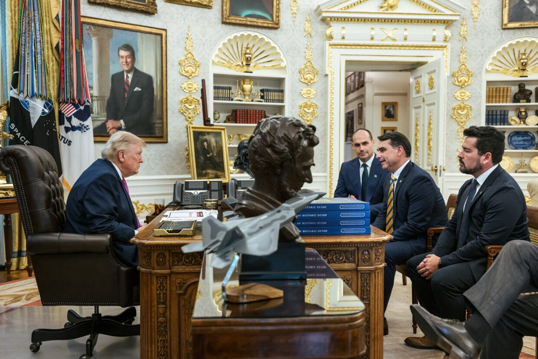 President Donald Trump seated at his desk in the Oval Office, with Brazilian senator Flávio Bolsonaro and two other men seated opposite