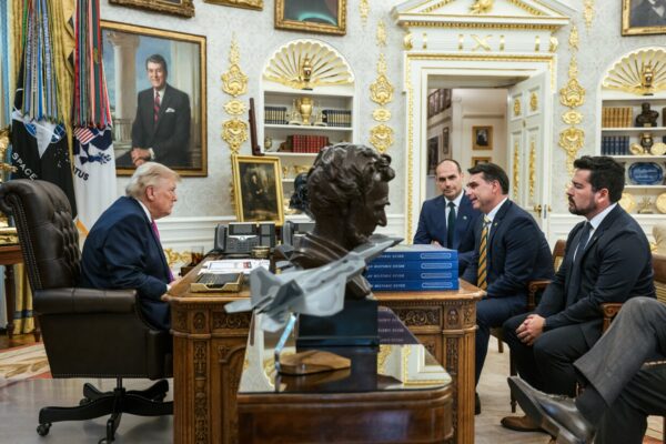President Donald Trump seated at his desk in the Oval Office, with Brazilian senator Flávio Bolsonaro and two other men seated opposite