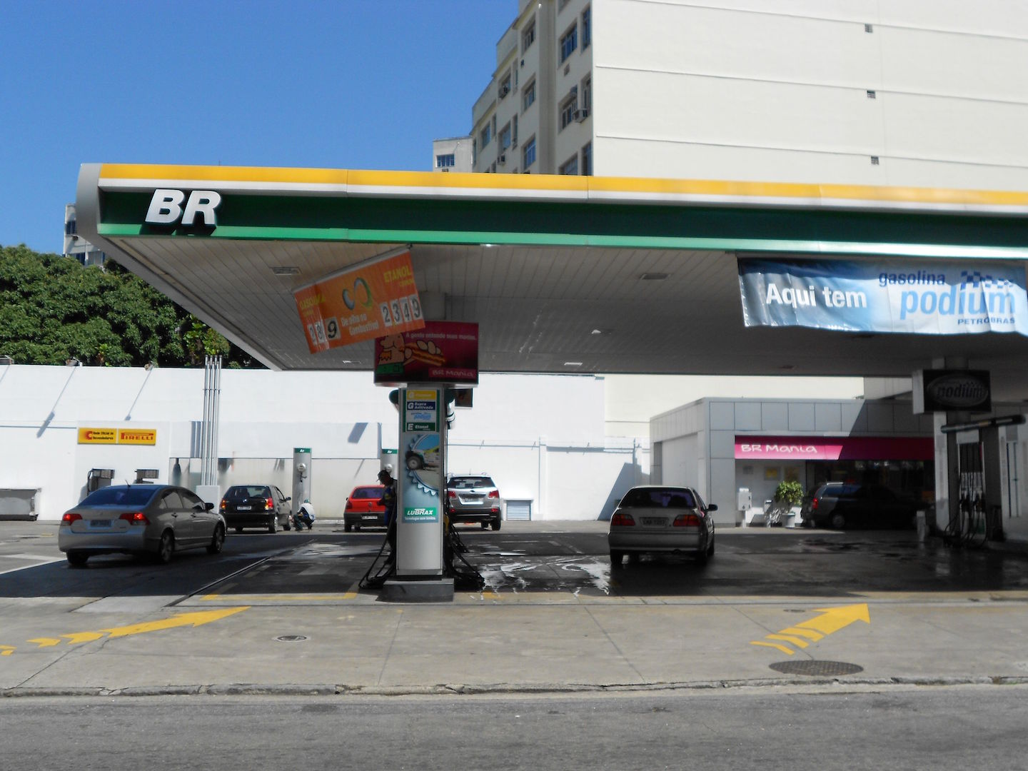 A service station under the green and yellow BR brand with cars at the pumps and a price board