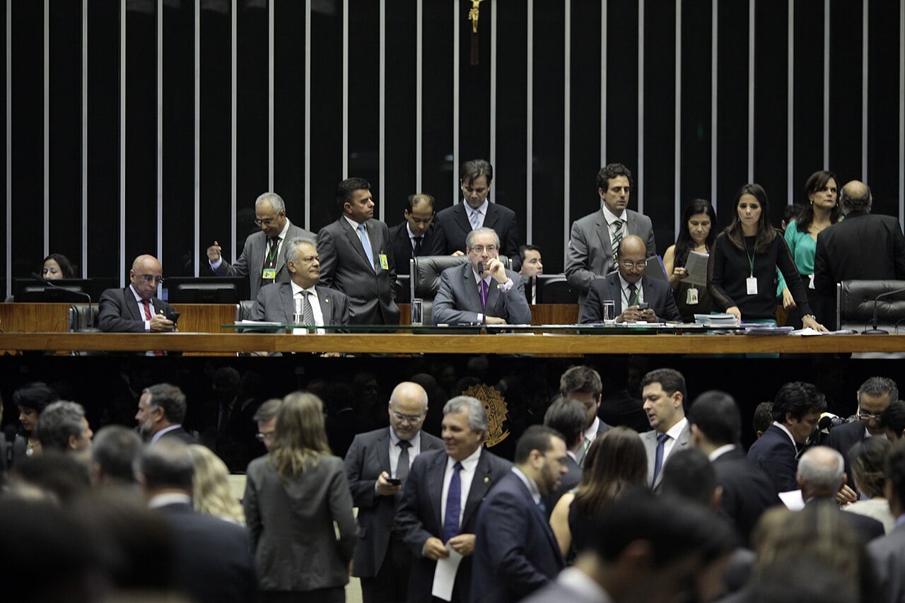Deputies standing and talking on the floor of Brazil's Chamber of Deputies in Brasília, below the presiding table