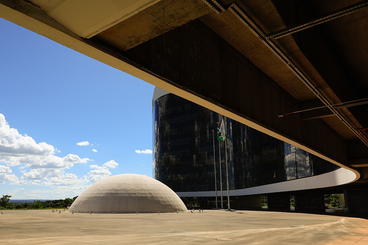 Dark glass tower and white dome of the electoral court headquarters under a blue sky