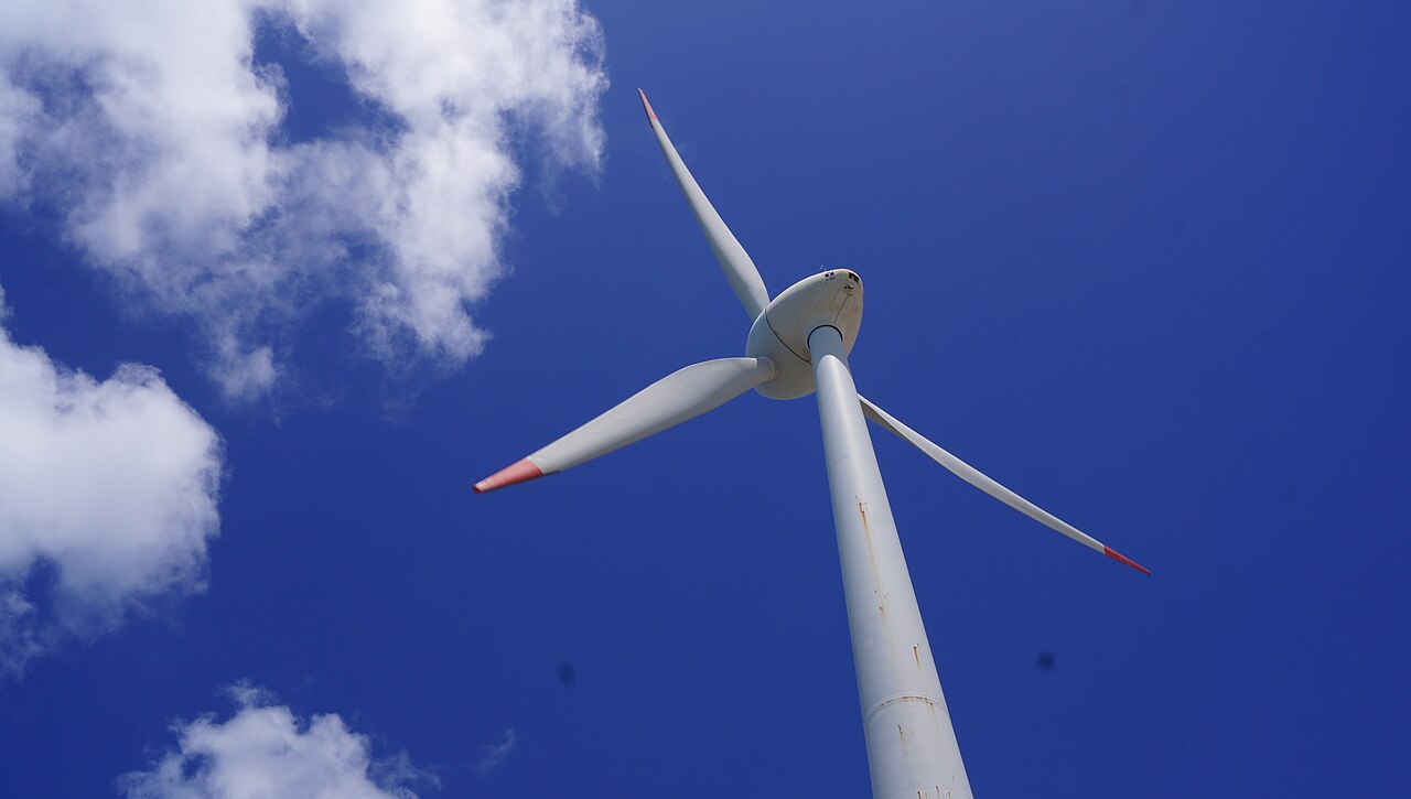 A wind turbine seen from below against a deep blue sky with white clouds in Fortaleza, Ceará