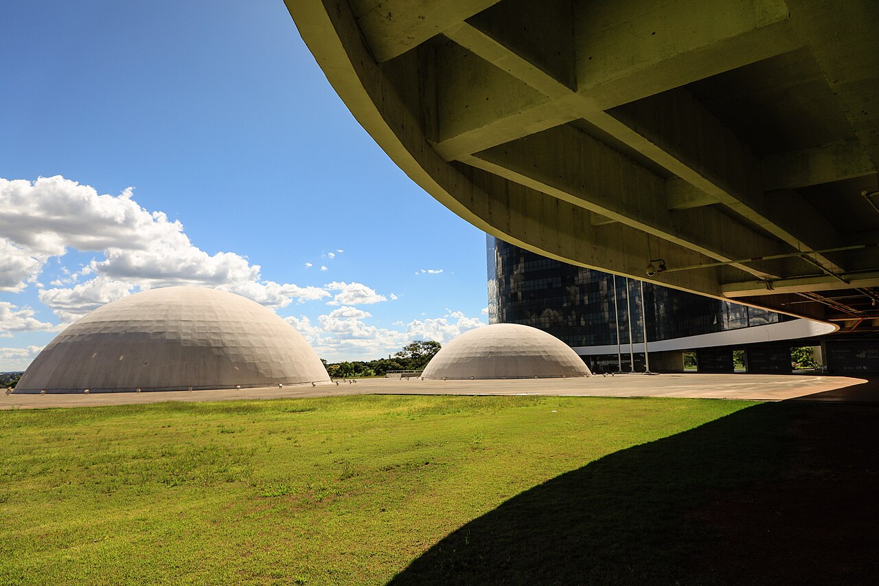 Two concrete domes and the curved underside of the Superior Electoral Court building in Brasília, with a lawn in the foreground