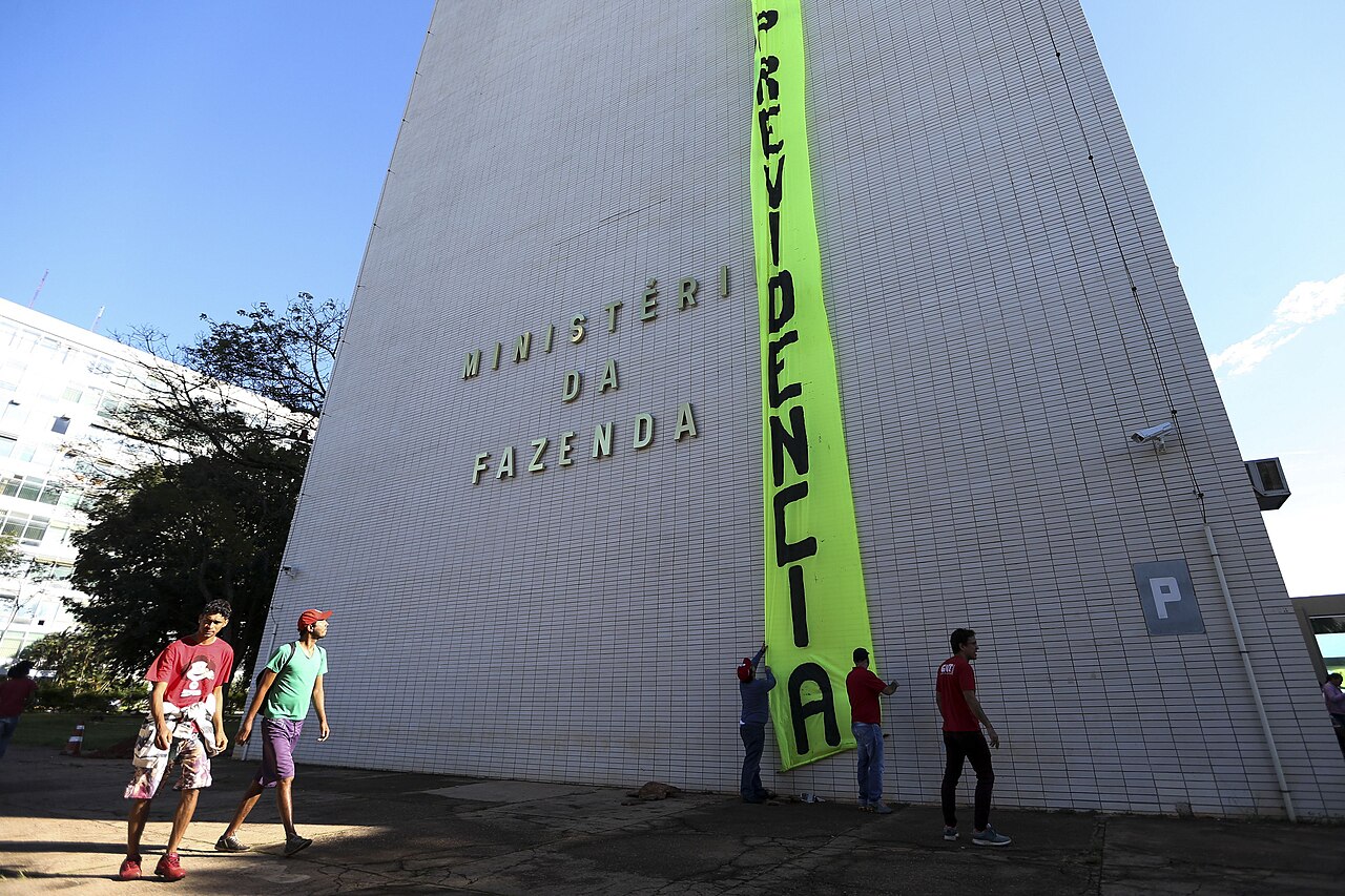 White tower of Brazil's Finance Ministry in Brasília with the ministry name in metal letters and people below a banner