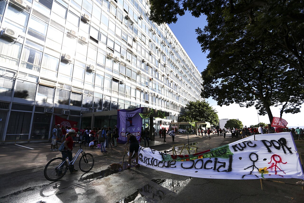 Glass-fronted Finance Ministry office block in Brasília with a crowd and banners in front