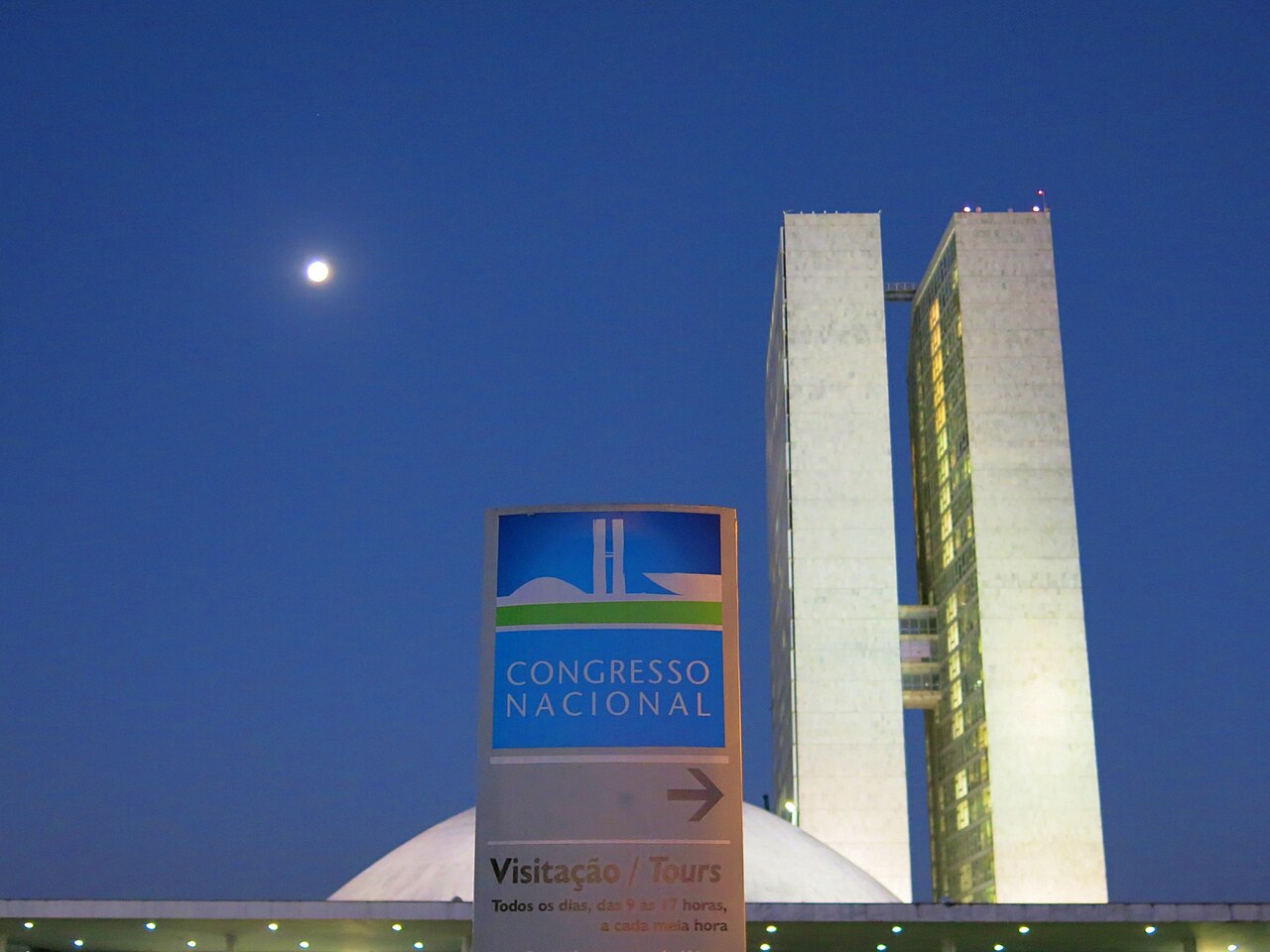 The twin towers and dome of Brazil's National Congress in Brasília at dusk, with a Congresso Nacional visitor sign and the moon