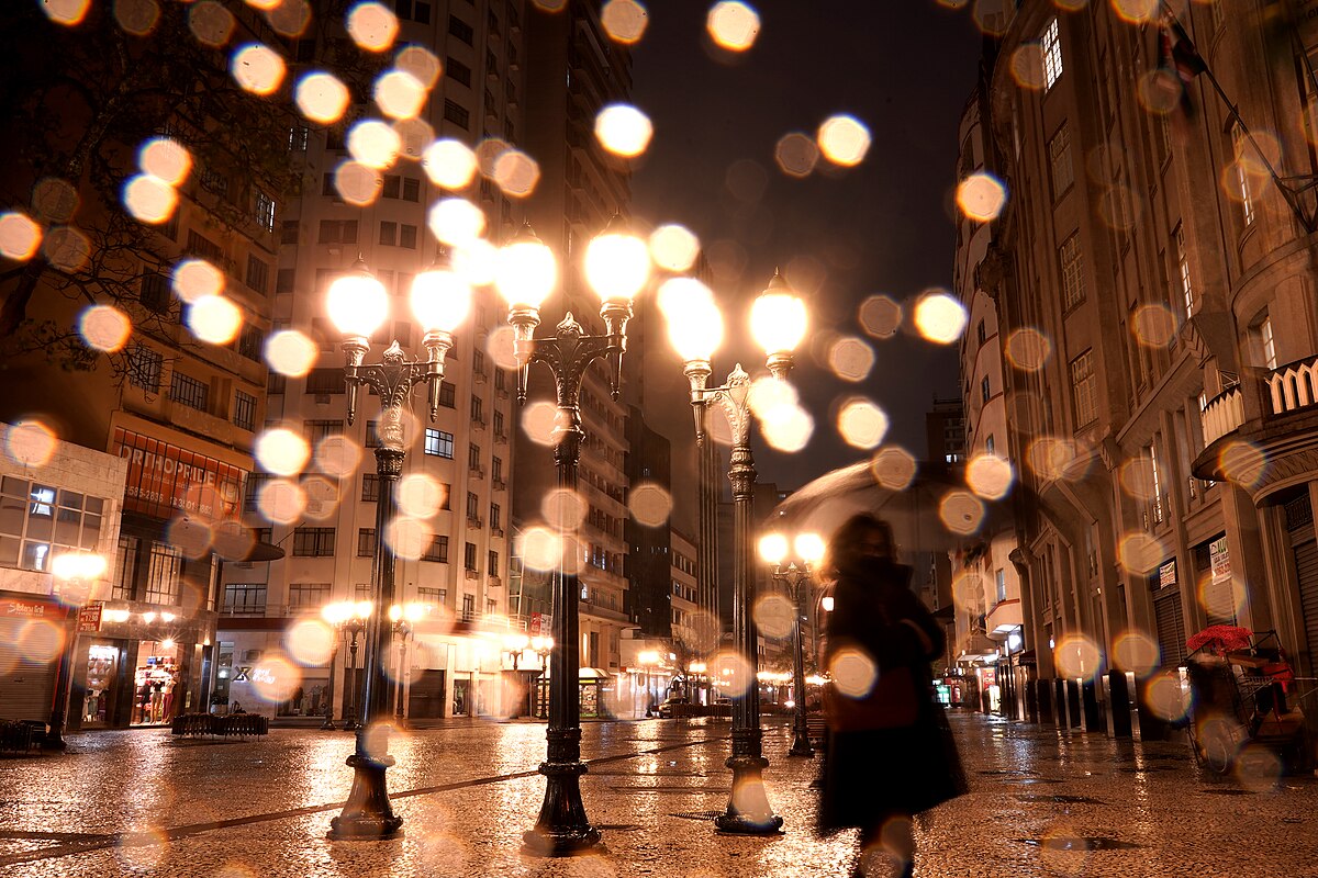 A pedestrian with an umbrella on a rainy night on Rua XV de Novembro in central Curitiba, Paraná, Brazil