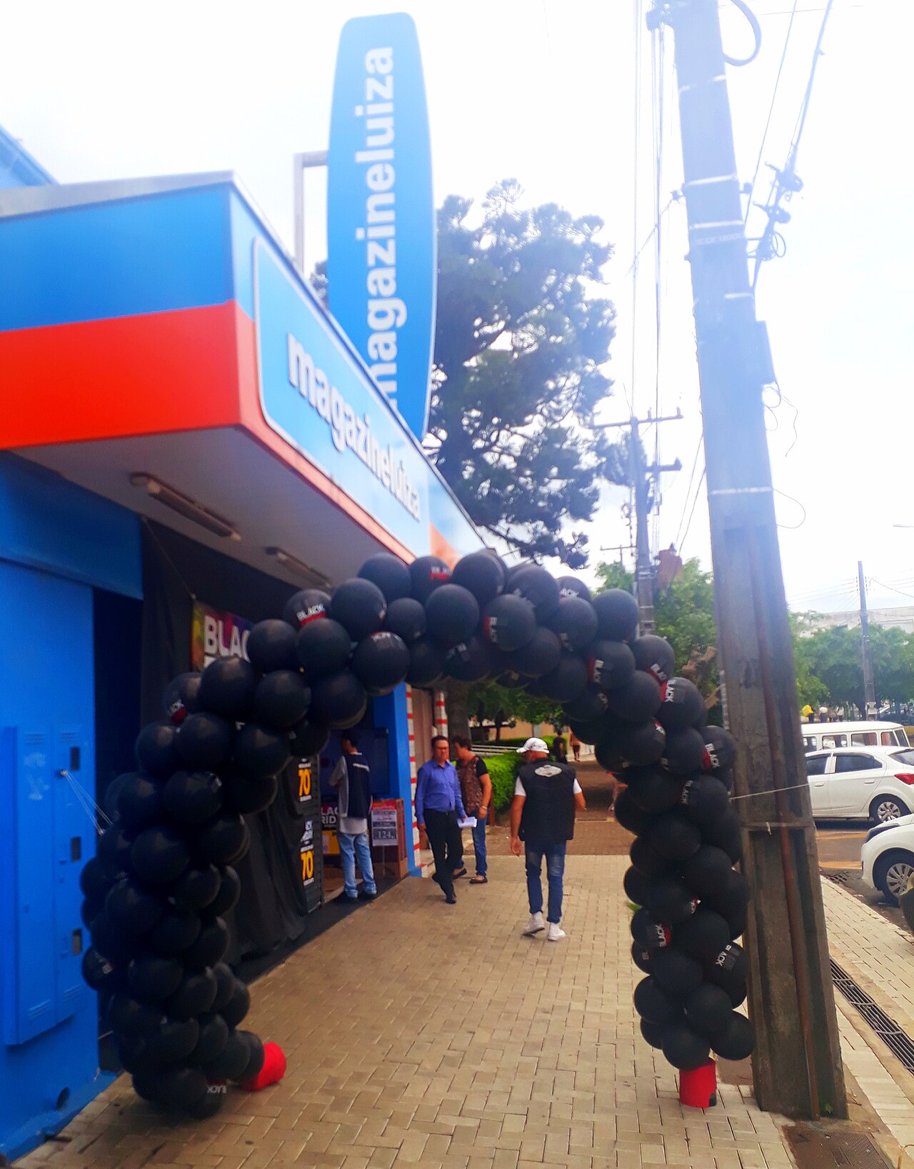 A Magazine Luiza shop front with a blue sign and an arch of black Black Friday balloons over the pavement