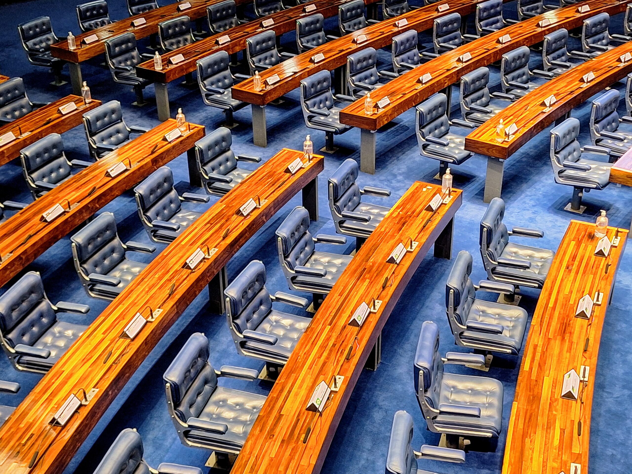 Rows of empty blue leather chairs and curved wooden desks in the Federal Senate plenary in Brasília