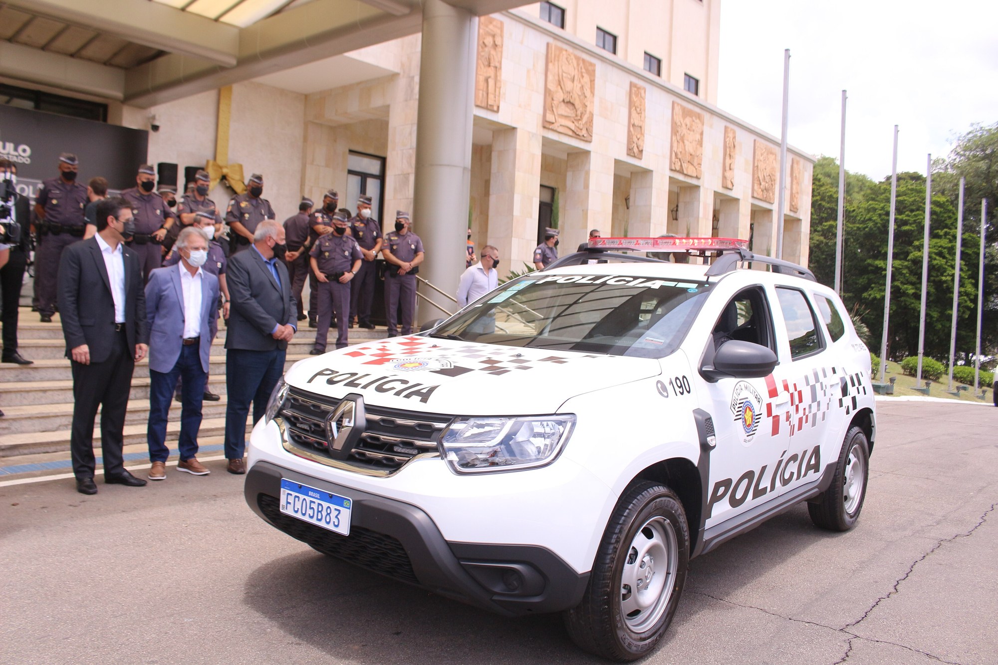A white São Paulo Military Police patrol car parked in front of uniformed officers