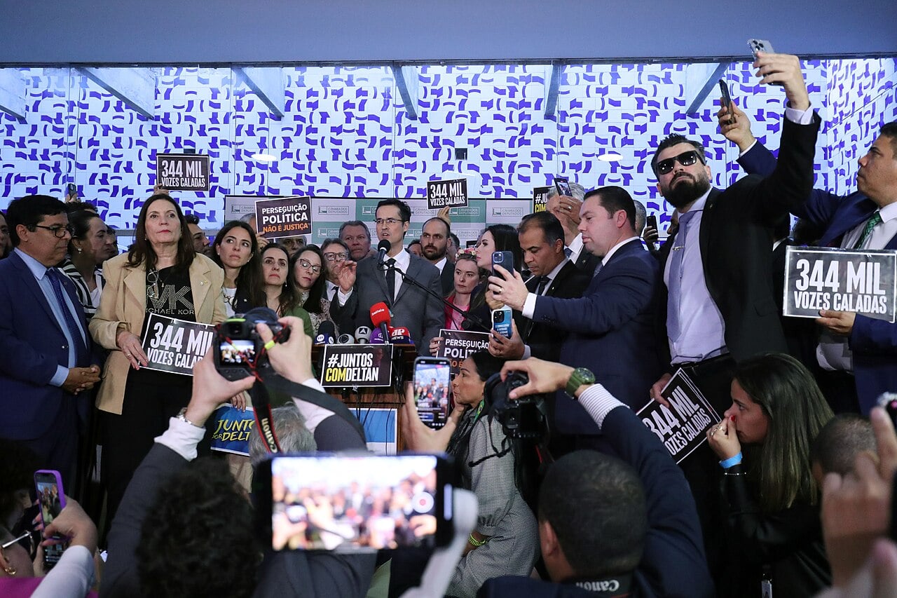 Deltan Dallagnol speaks at a bank of microphones in Brazil's Congress, surrounded by supporters holding signs reading 344 mil vozes caladas
