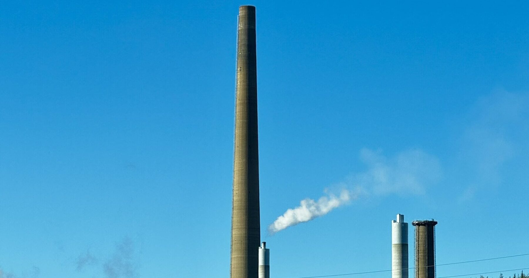 A tall smelter chimney and two smaller stacks under a clear blue sky at the Copper Cliff smelter complex in Sudbury, Ontario