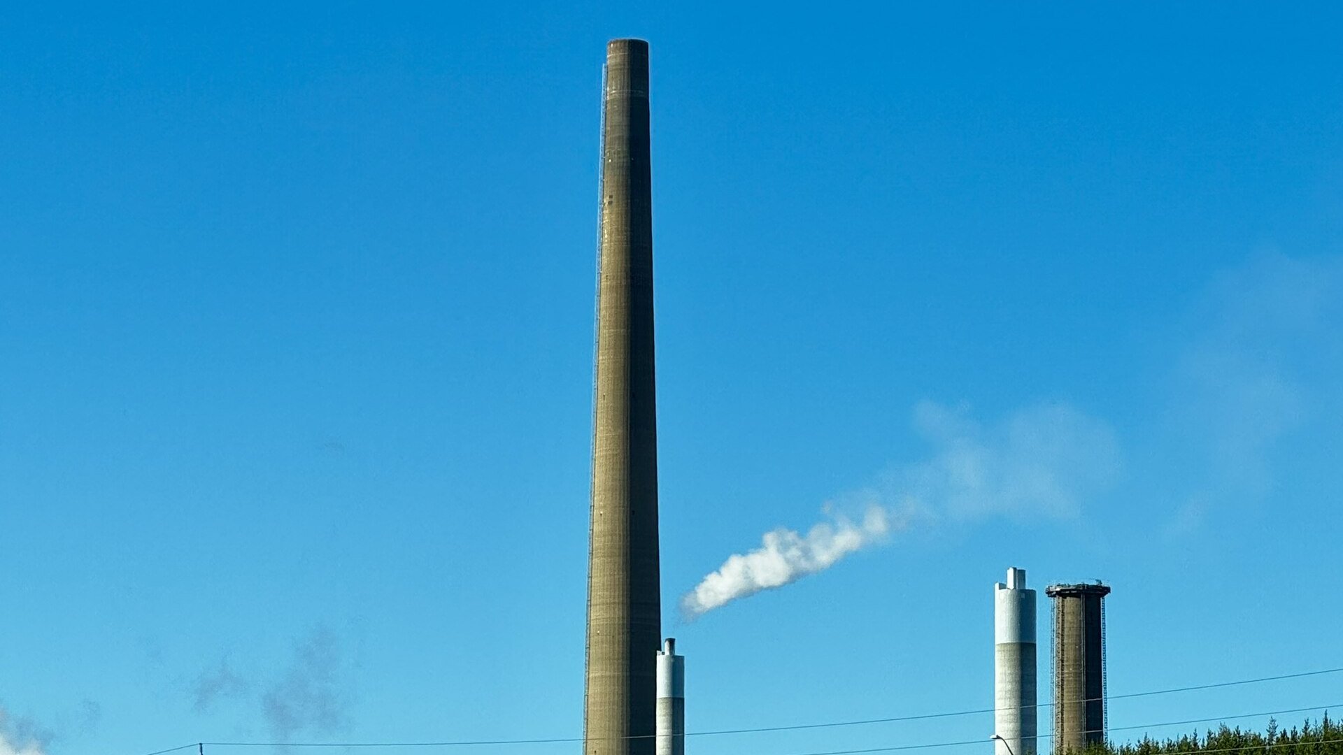 A tall smelter chimney and two smaller stacks under a clear blue sky at the Copper Cliff smelter complex in Sudbury, Ontario