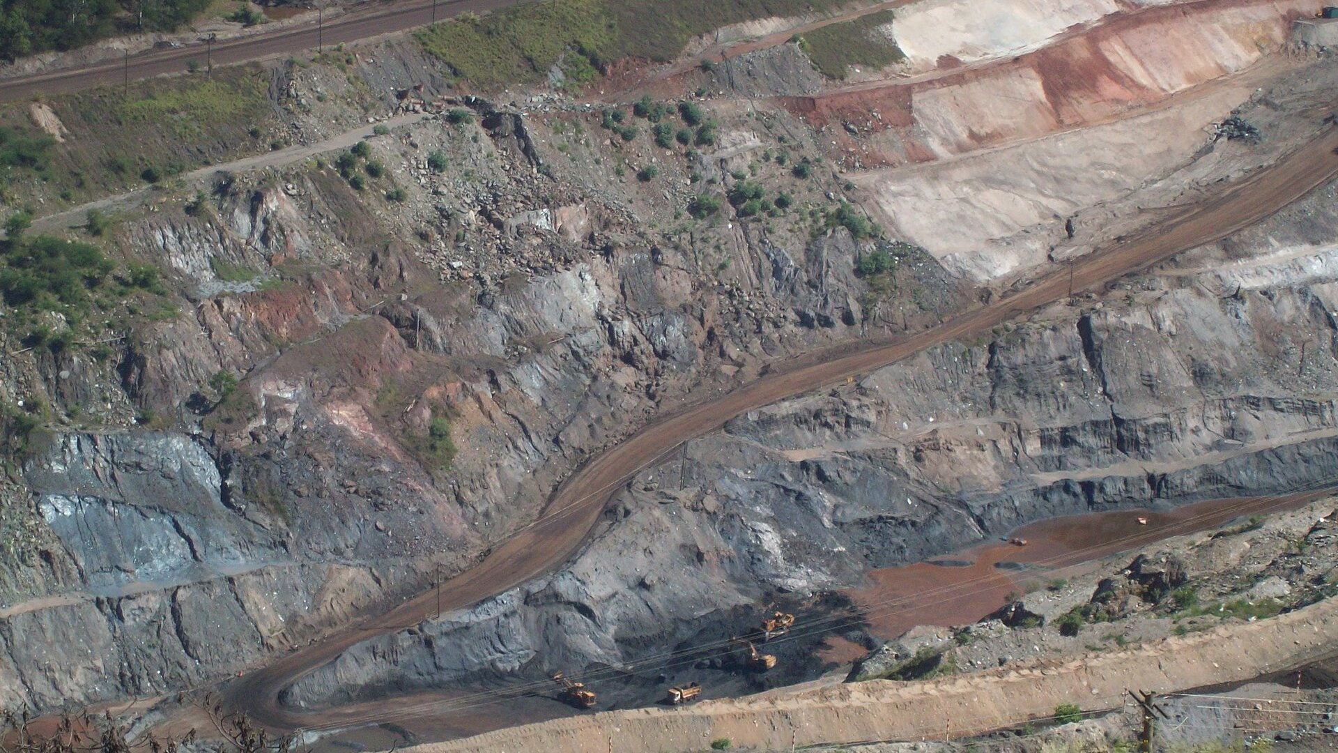 Trucks and excavators working the benches of a large open-pit iron ore mine run by Vale in Itabira, Minas Gerais