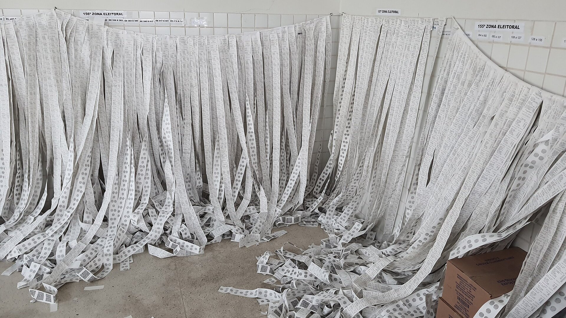 Strips of printed vote tally slips from Brazilian electronic voting machines hang by electoral zone on a tiled wall in Feira de Santana