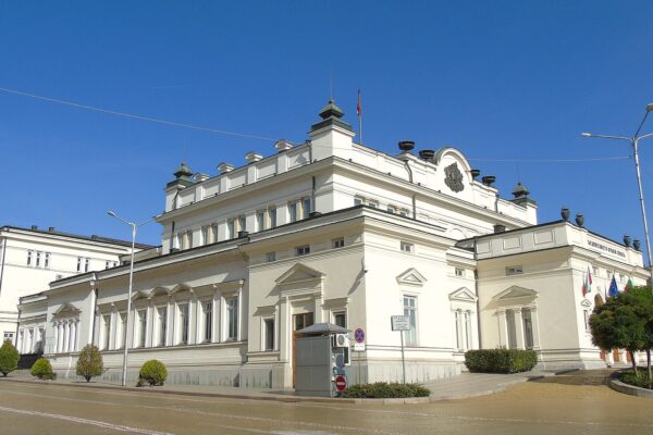 The white National Assembly building in Sofia, Bulgaria, seen from the corner of the street under a blue sky
