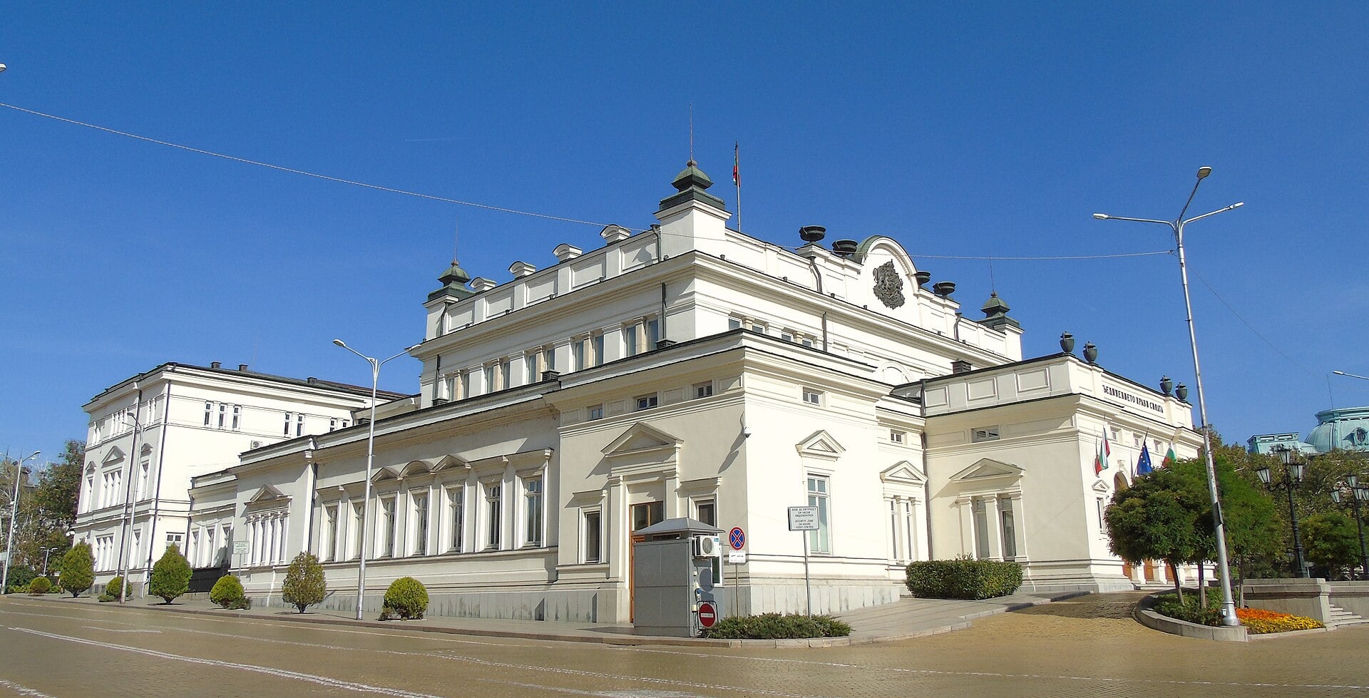 The white National Assembly building in Sofia, Bulgaria, seen from the corner of the street under a blue sky