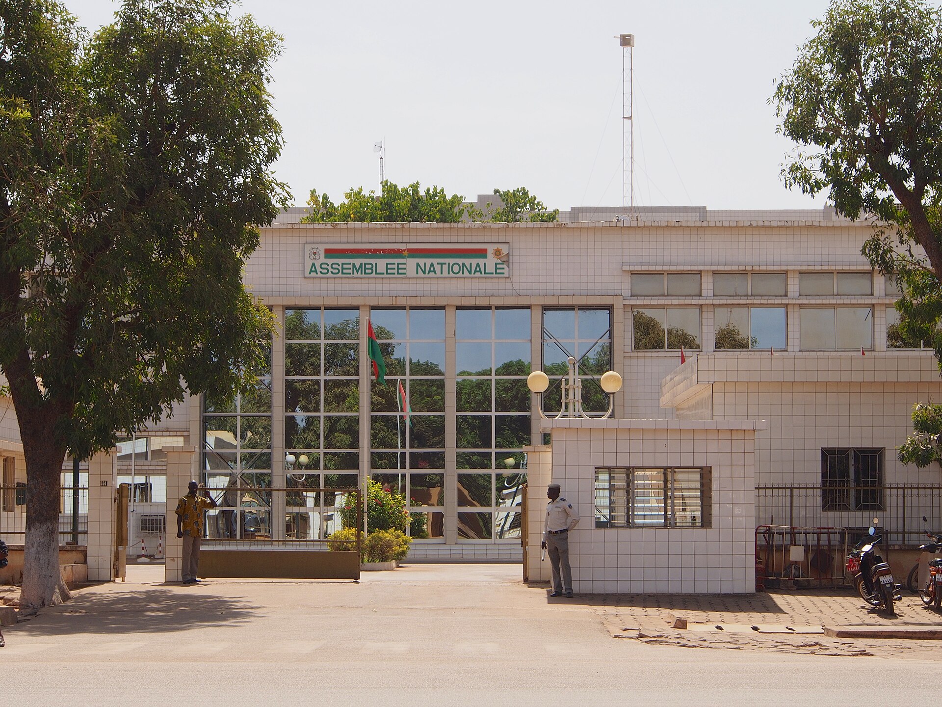 White tiled building with the sign Assemblee Nationale and two men at the gate in Ouagadougou, Burkina Faso