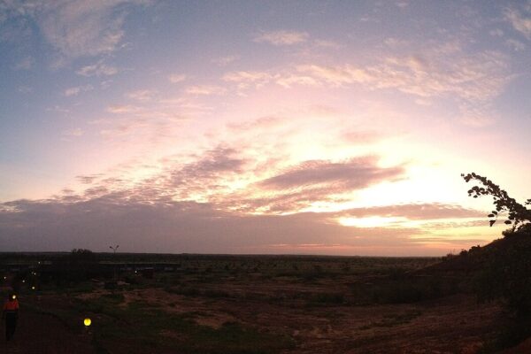 Sunrise over a gold mine site in northern Burkina Faso, with a worker in an orange jacket walking beside lit paths