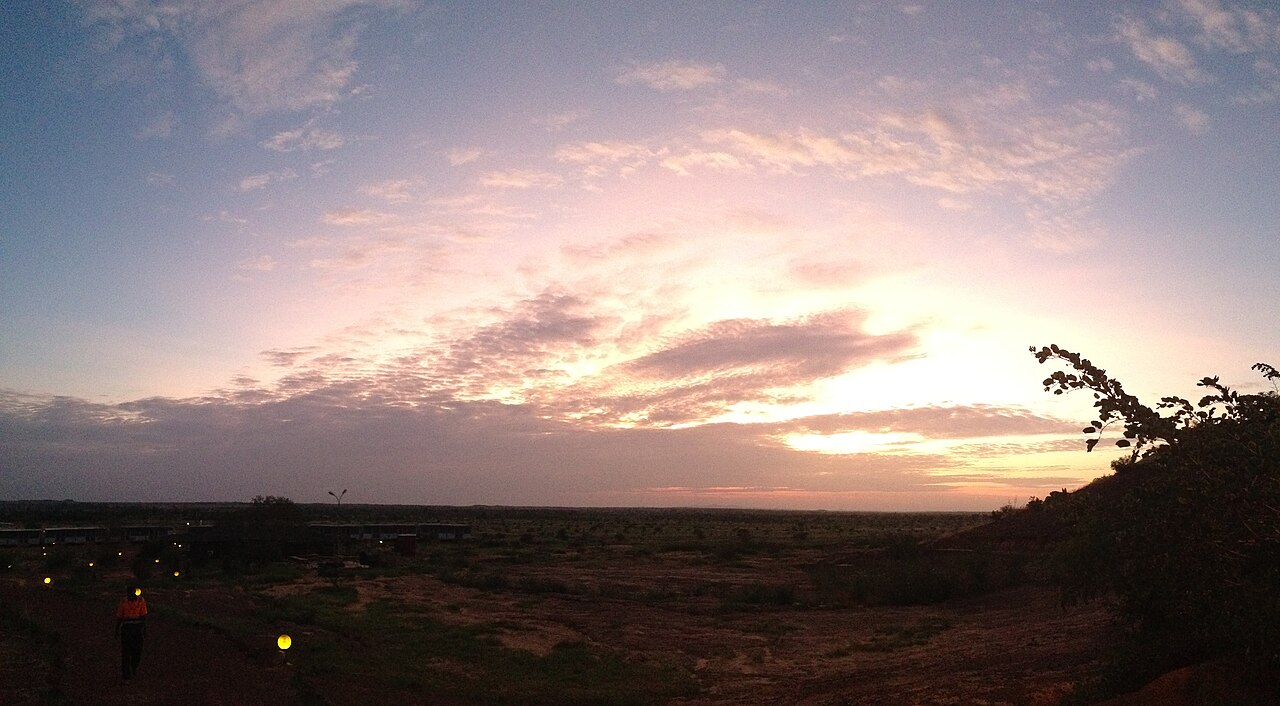 Sunrise over a gold mine site in northern Burkina Faso, with a worker in an orange jacket walking beside lit paths