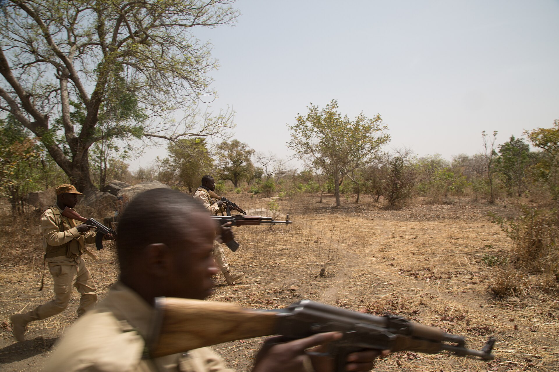 Burkinabe soldiers with rifles move through dry bush during a training exercise