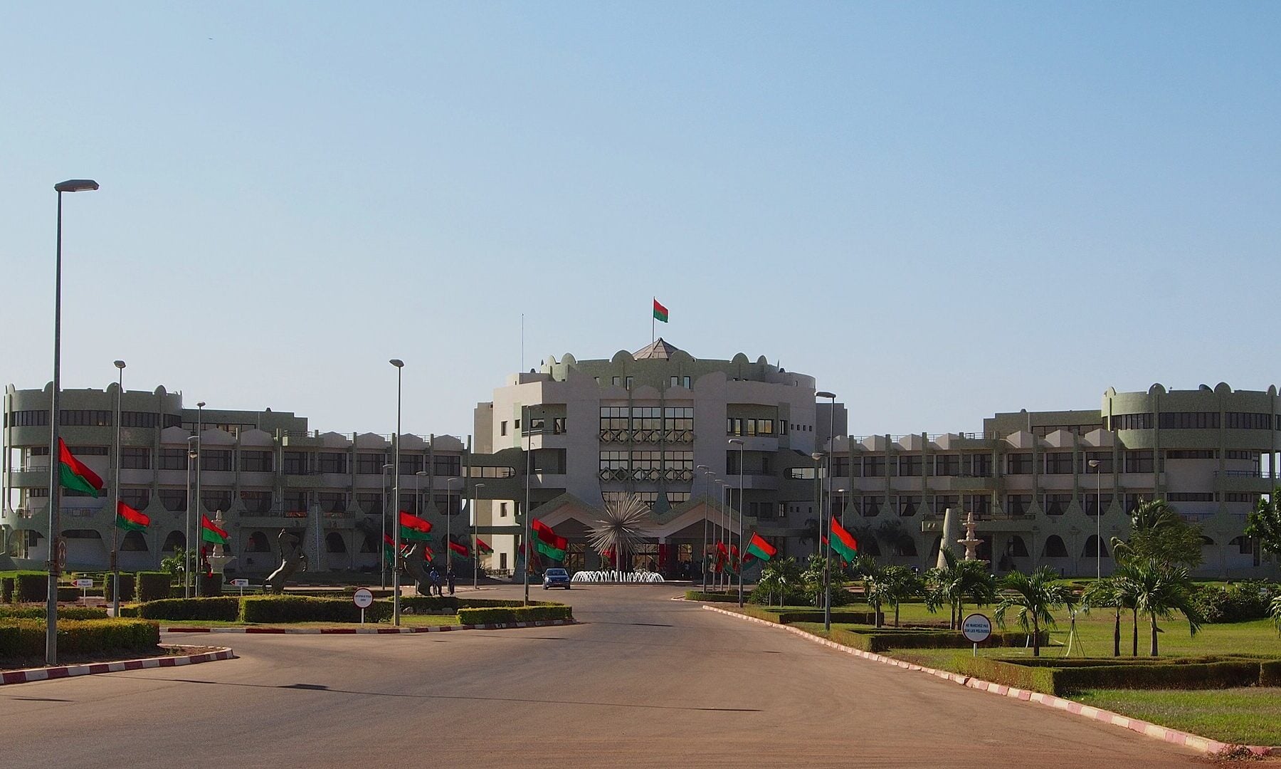 The Kosyam presidential palace in Ouagadougou, a long pale building with a central tower and red and green Burkina Faso flags along the drive
