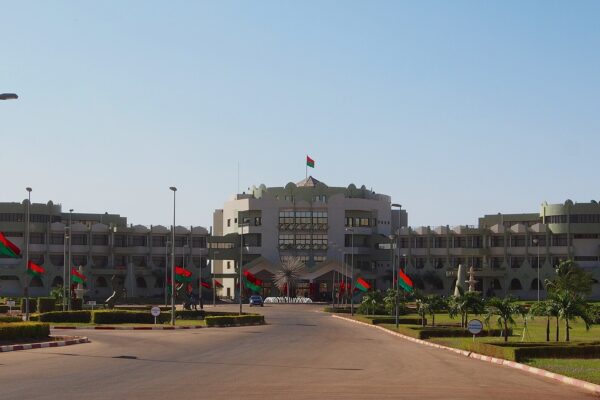 The Kosyam presidential palace in Ouagadougou, a long pale building with a central tower and red and green Burkina Faso flags along the drive