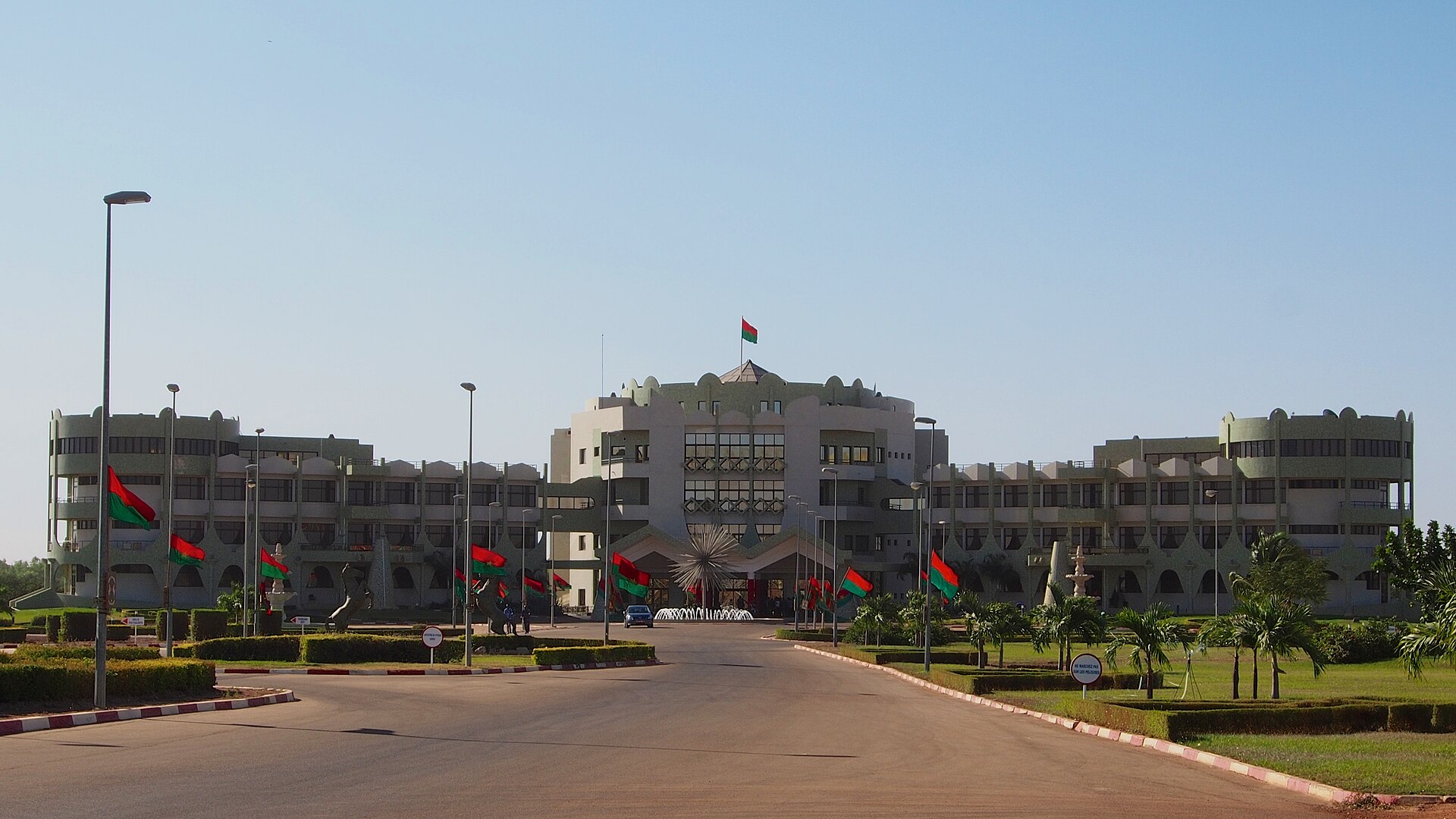 The Kosyam presidential palace in Ouagadougou, a long pale building with a central tower and red and green Burkina Faso flags along the drive