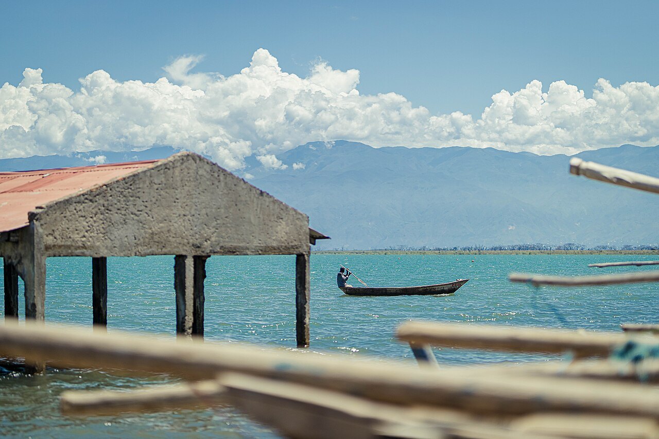 A fisherman paddles a dugout canoe on the turquoise water of Lake Tanganyika, with mountains in the distance