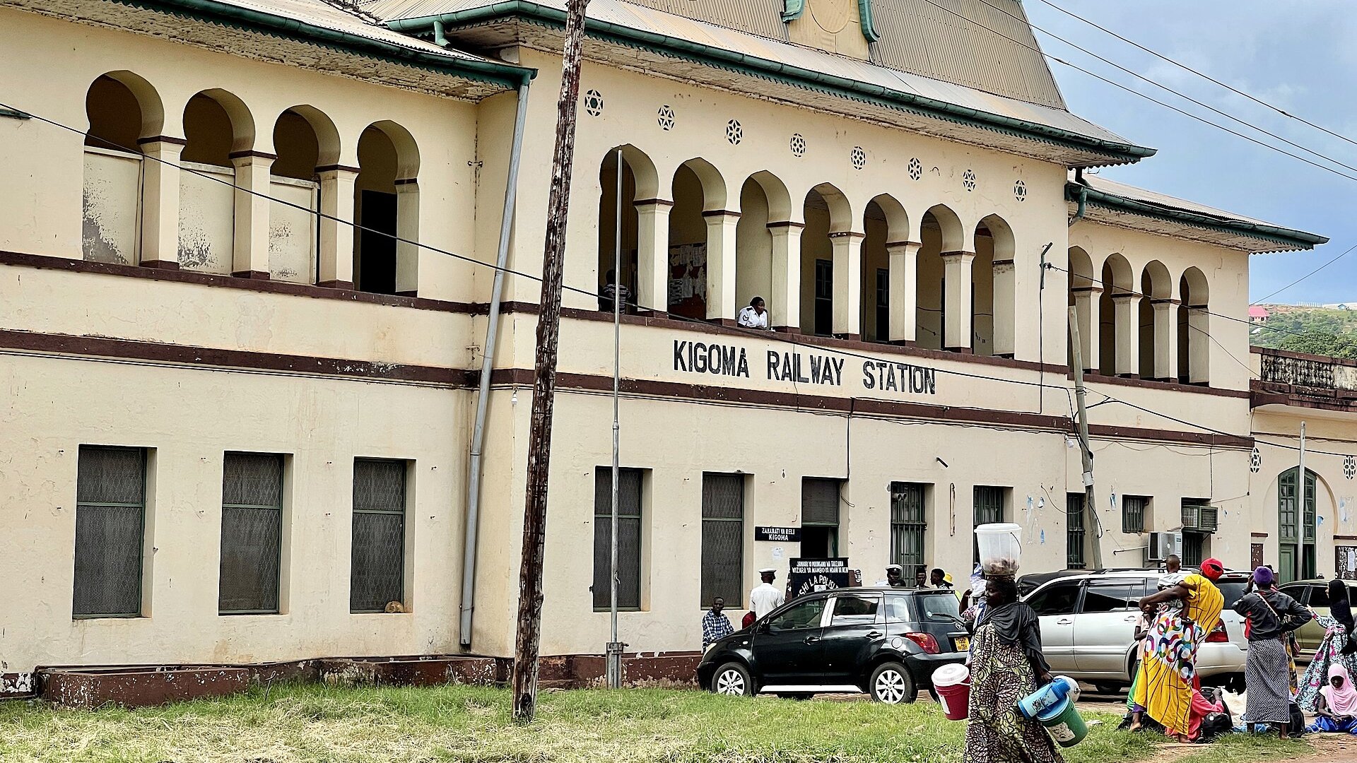 The old colonial-era Kigoma railway station in Tanzania, with women carrying goods past the building.