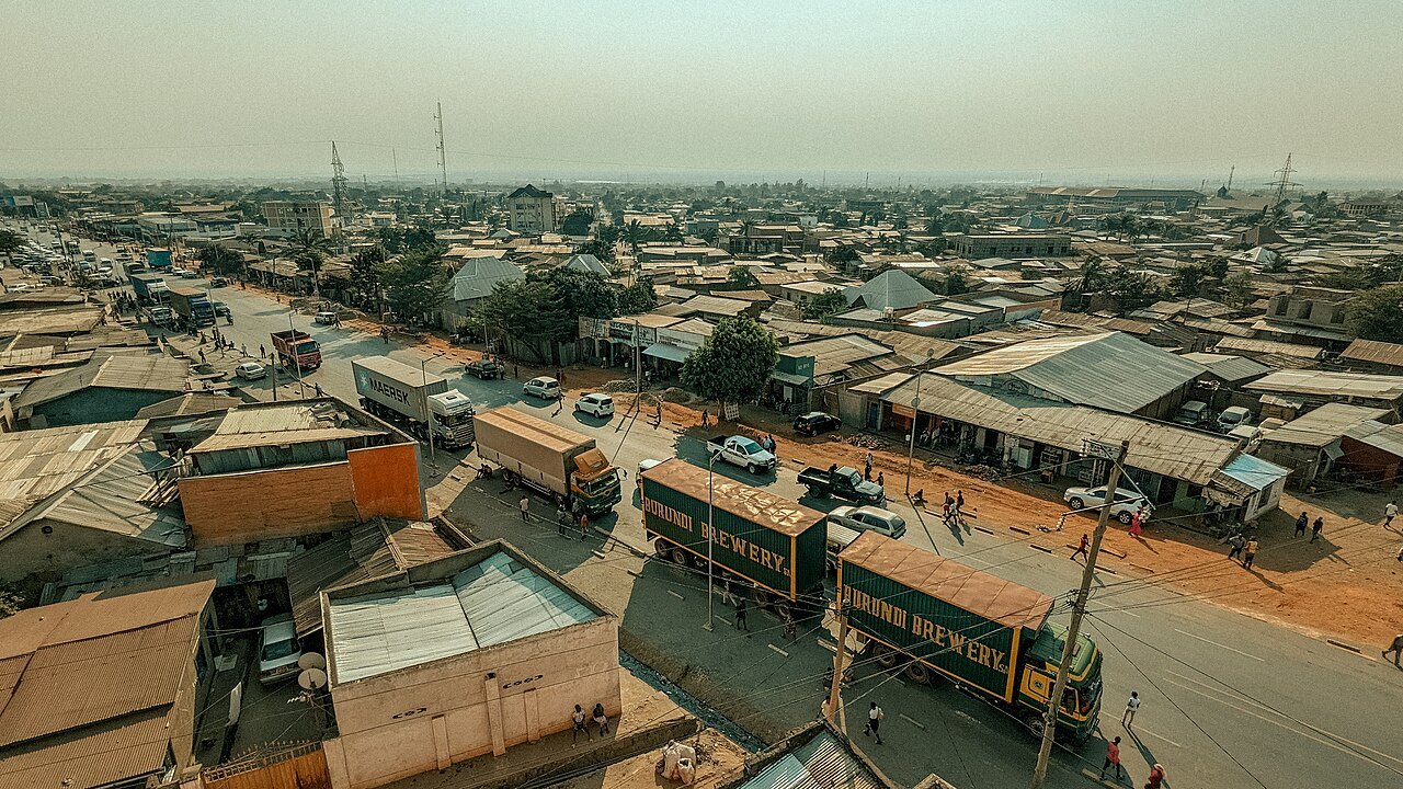 Aerial view of a busy road in Bujumbura, Burundi, with brewery lorries, shops with corrugated roofs and pedestrians