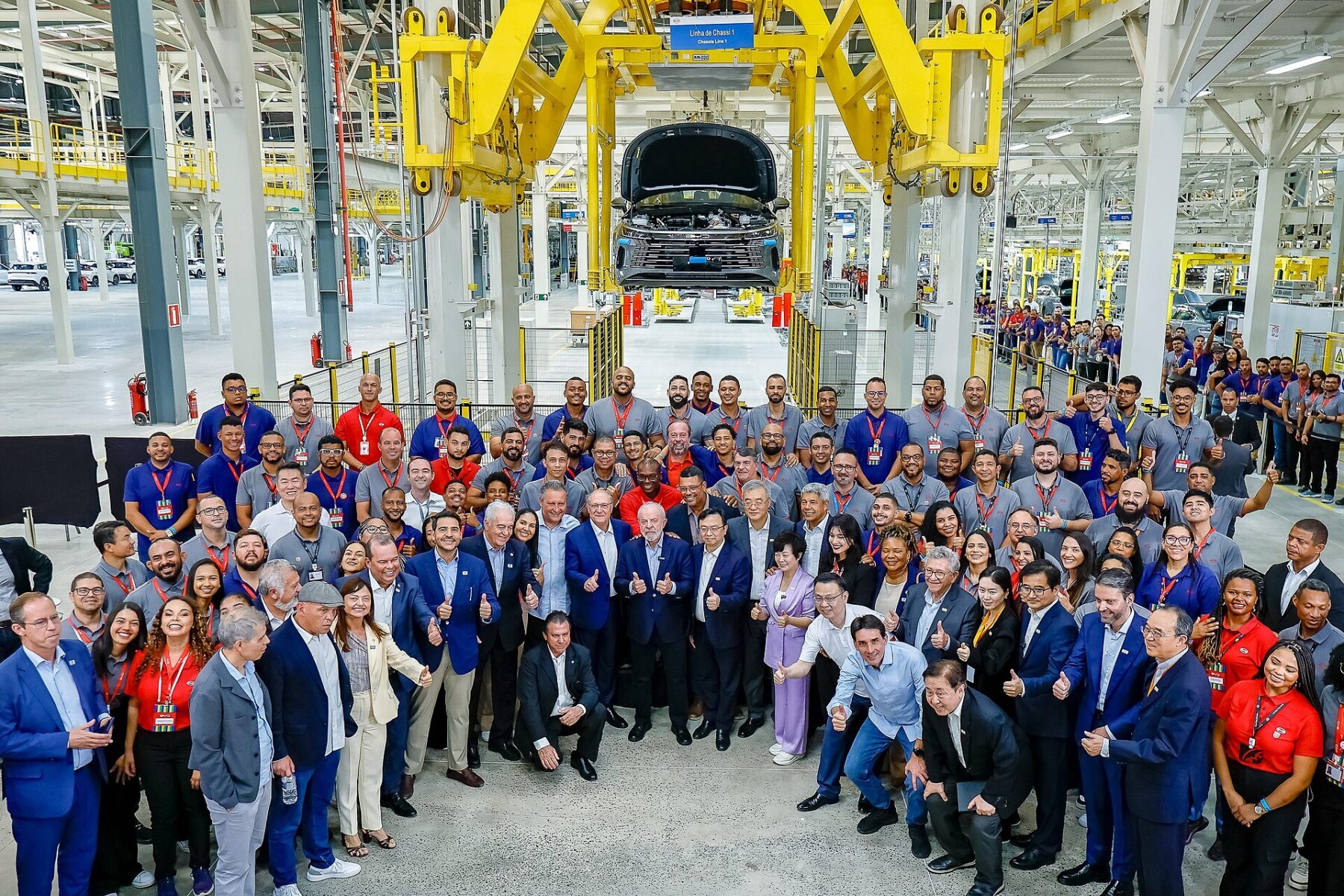 Workers and guests gather beneath a chassis line at the BYD car factory in Camaçari, Bahia state, Brazil