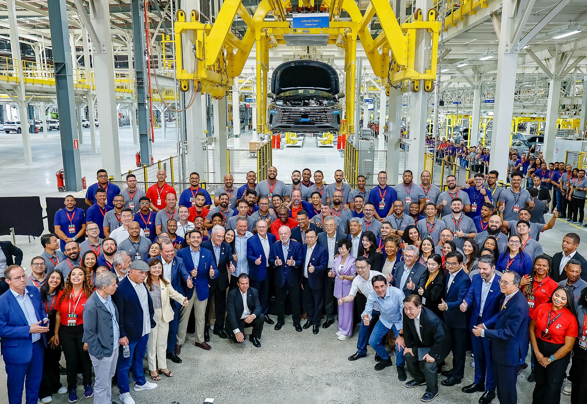 Workers and guests gather beneath a chassis line at the BYD car factory in Camaçari, Bahia state, Brazil