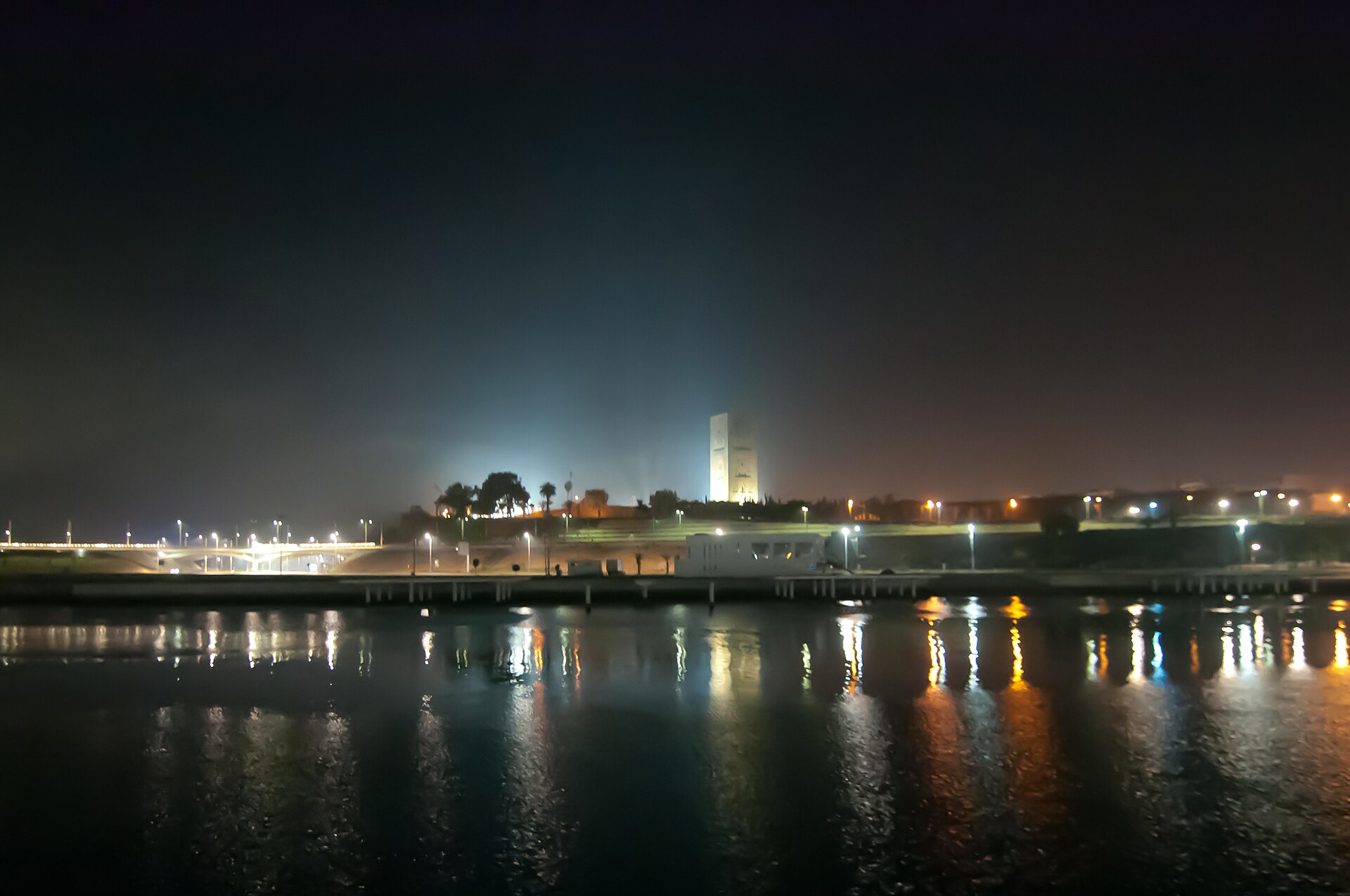 The floodlit Hassan Tower on a hill above the Bouregreg River at night, with lights reflected in the water