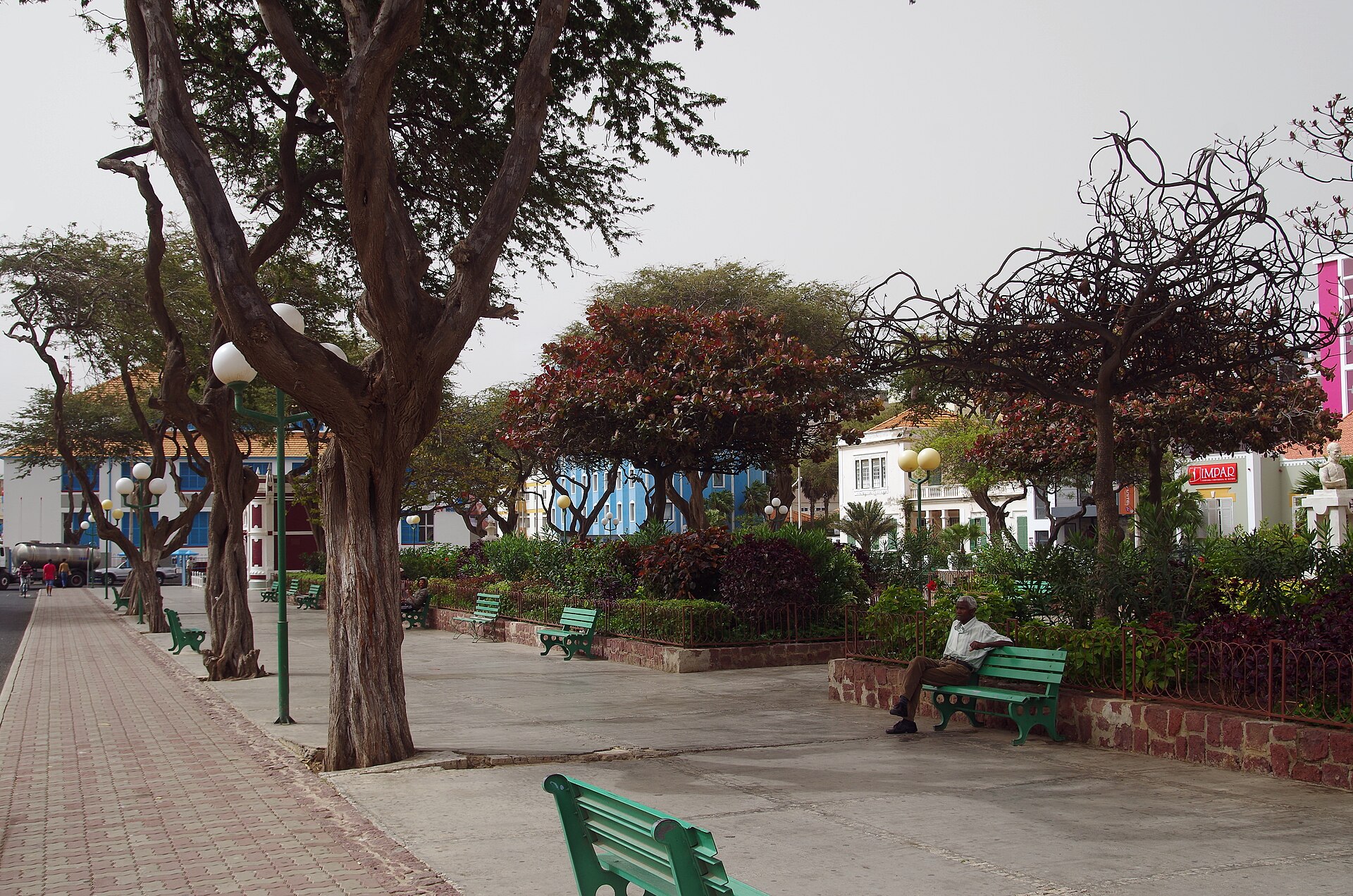 Tree-lined Praça Nova square in Mindelo, Cabo Verde, with green benches and colonial-era buildings